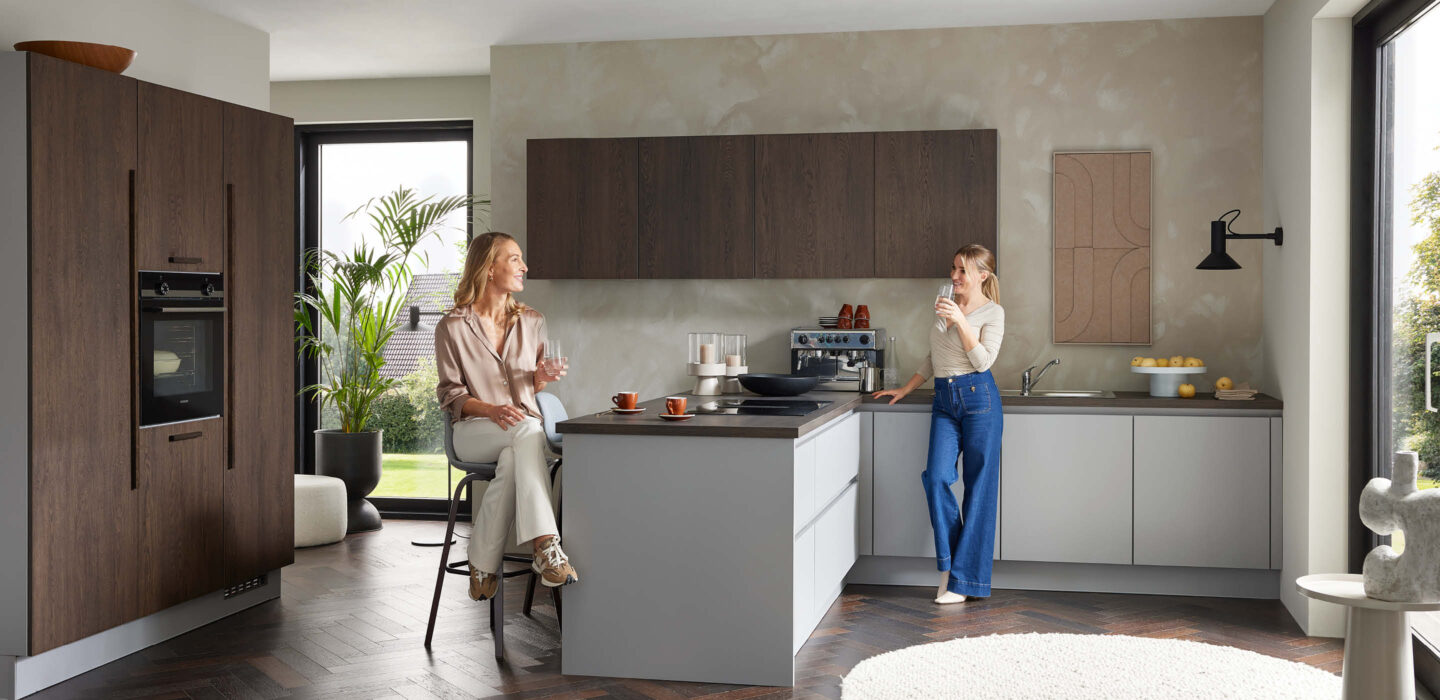 Zeitlose Burger Küche bei H&L Küchenstudio in Emlichheim mit Kombination aus dunklem Holz und hellen Fronten, Kücheninsel und zwei Personen im Gespräch in wohnlicher Atmosphäre